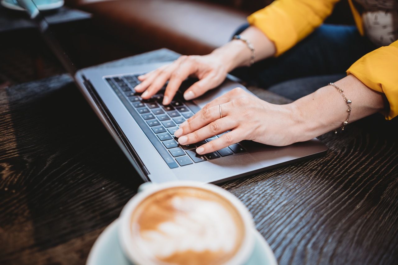 a woman engrossed in work, typing on a laptop while savoring a cup of coffee